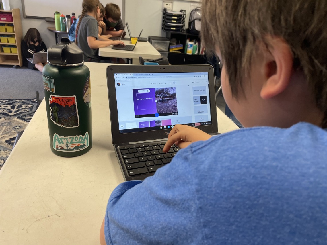 Fourth grade student sitting in front of an open laptop. Student is typing on the laptop.