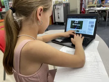 Third grade student typing on an open laptop in front of them.